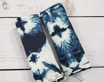Könnte beinhalten: Zwei mit Stoff bezogene Griffe mit einem blauen und weißen Batik-Muster. Die Griffe sind mit weißem Garn genäht und haben ein weiches, flauschiges Futter. Die Griffe befinden sich auf einer weißen Holzoberfläche. Der Text "J.J.C.oties - HANDMADE" ist in der rechten unteren Ecke des Bildes sichtbar.