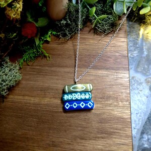 May include: A silver chain necklace with a charm of three stacked blue and green books with white designs. The books are painted to look like old, worn books.