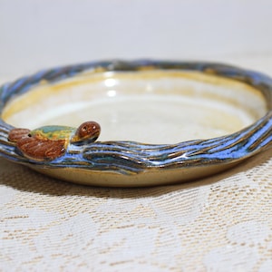 May include: A ceramic dish with a blue and brown glaze, featuring a small turtle figurine on the rim. The dish is round and has a slightly raised edge.
