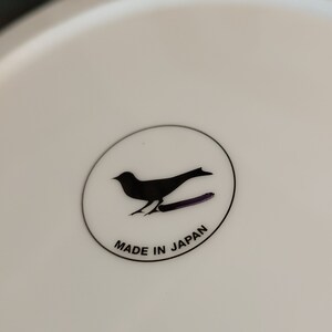 K&ouml;nnte beinhalten: Ein wei&szlig;er Keramikteller mit einer schwarzen Silhouette eines Vogels und dem Text "MADE IN JAPAN" in einem Kreis.