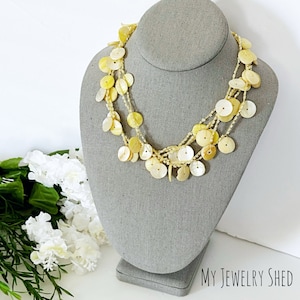 May include: A multi-strand necklace with yellow-toned shell discs and small beads. The necklace is displayed on a gray mannequin bust. The text "MY JEWELRY SHED" is visible in the lower right corner.