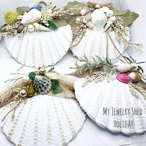 May include: Four white seashell ornaments decorated with seashells, beads, and dried flowers. The ornaments are arranged on a white surface. The text "My Jewelry Shed Holiday" is visible in the bottom right corner of the image.