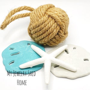 May include: A set of three nautical-themed decorations, including a beige rope knot, a light blue seashell, and a white starfish. The text "MY JEWELRY SHED HOME" is visible in the bottom left corner of the image.