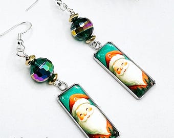 May include: Dangle earrings featuring a rectangular pendant with a Santa Claus illustration. The earrings have a silver-tone hook, a faceted green bead, and gold-tone accents. The text "My Jewelry Shed" is at the bottom.