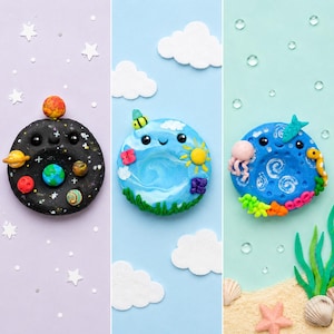 May include: Three colourful clay donut-shaped creations. One is a black galaxy with planets, another is a blue Earth with a smiling face, and the last is a blue ocean scene with an octopus and seahorse. The background features stars, clouds, and sand.