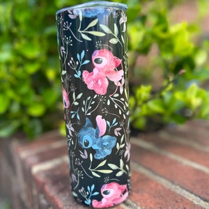 May include: A black stainless steel tumbler with a floral pattern featuring pink and blue cartoon characters. The tumbler has a clear lid.