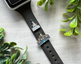 Puede incluir: Una correa de reloj negra con dos dijes de castillo de oro y esmalte. Los dijes son de un castillo de cuento de hadas con detalles azules.