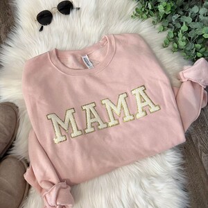May include: A pink sweatshirt with the word "MAMA" in gold glitter letters.