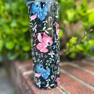 May include: A black stainless steel tumbler with a floral pattern and cartoon characters. The characters are blue, pink, and white. The tumbler has a lid.