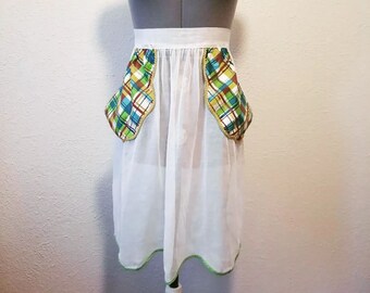 Pode incluir: Avençal branco com bolsos xadrez verdes e marrons. O avental tem uma cintura branca e uma bainha verde ao redor da parte inferior.