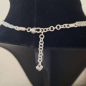 Pode incluir: Colar de corrente de prata com fecho em forma de cora&ccedil;&atilde;o. O colar est&aacute; sobre um fundo de veludo preto.
