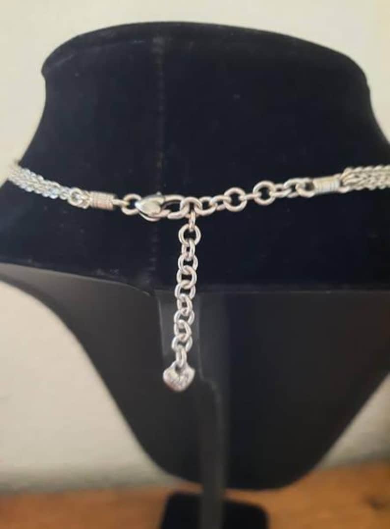 Pode incluir: Colar de corrente de prata com fecho em forma de cora&ccedil;&atilde;o. O colar est&aacute; sobre um fundo de veludo preto.