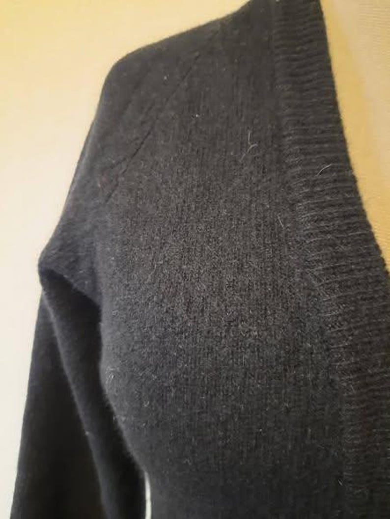 May include: Close-up of a black V-neck sweater. The sweater is made of a soft, textured material. The image focuses on the shoulder and upper chest area, highlighting the fabric's weave and the garment's construction.