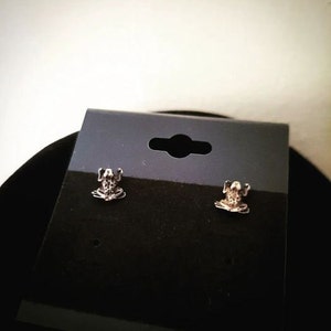 May include: A pair of silver frog stud earrings on a black display card.