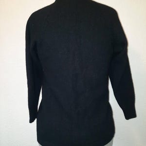May include: A black sweater with long sleeves and a crew neck. The sweater is displayed on a mannequin. The fabric appears to be a soft knit. The sleeves are three-quarter length.