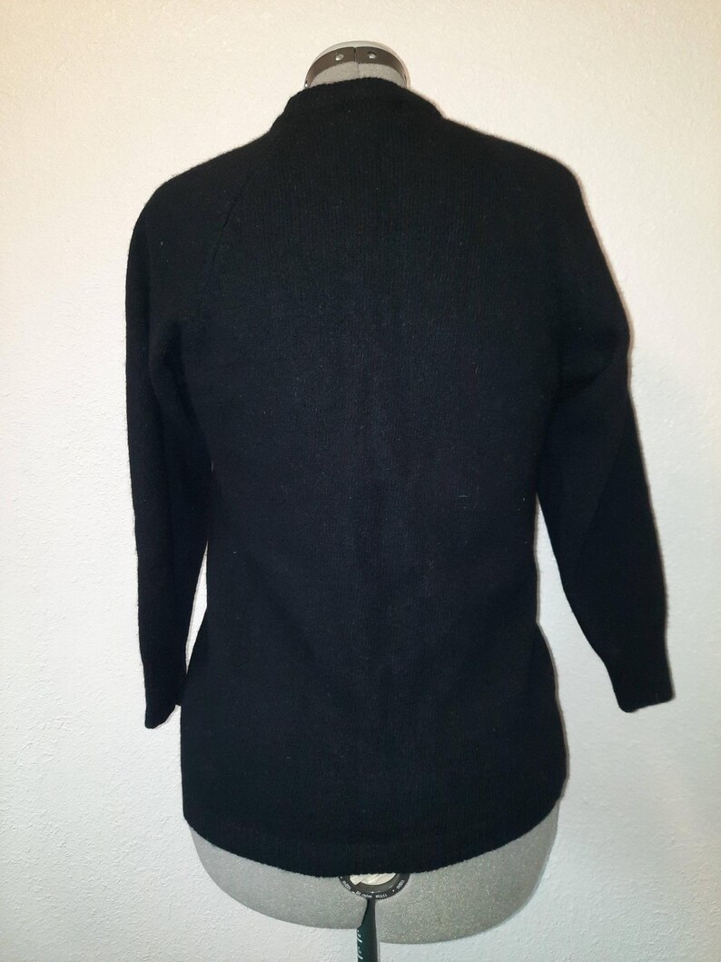May include: A black sweater with long sleeves and a crew neck. The sweater is displayed on a mannequin. The fabric appears to be a soft knit. The sleeves are three-quarter length.