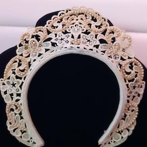 May include: An off-white lace collar with pearl and rhinestone accents. The collar is circular, with intricate floral and scrollwork designs. The collar is displayed on a black surface.