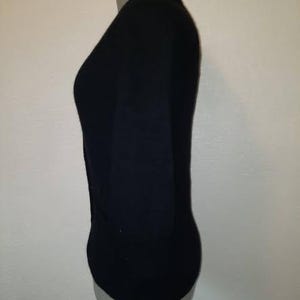 May include: A black, long-sleeved top displayed on a mannequin. The top has a V-neck and appears to be made of a soft, form-fitting material. The mannequin is a neutral color, and the background is a plain white wall.