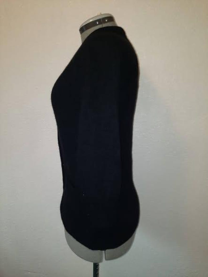 May include: A black, long-sleeved top displayed on a mannequin. The top has a V-neck and appears to be made of a soft, form-fitting material. The mannequin is a neutral color, and the background is a plain white wall.