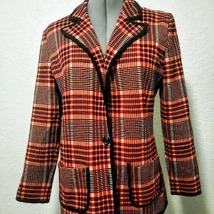 May include: A vintage blazer in a red, black, and cream plaid pattern. The blazer has a notched collar, two front pockets, and a single-button closure. Black trim outlines the collar, pockets, and front edges.