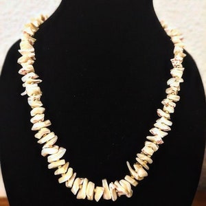 Puede incluir: Un collar de conchas blancas con detalles dorados. El collar está hecho de pequeñas conchas de forma irregular.