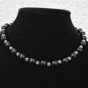 Peut inclure: Un collier de perles noires avec des accents argent&eacute;s. Les perles sont rondes et ont une surface l&eacute;g&egrave;rement textur&eacute;e.