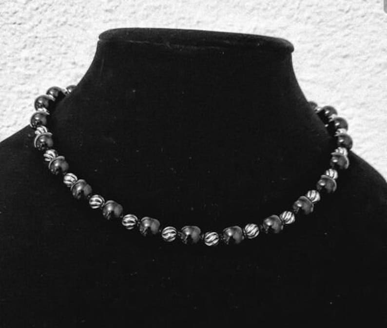 Peut inclure: Un collier de perles noires avec des accents argent&eacute;s. Les perles sont rondes et ont une surface l&eacute;g&egrave;rement textur&eacute;e.