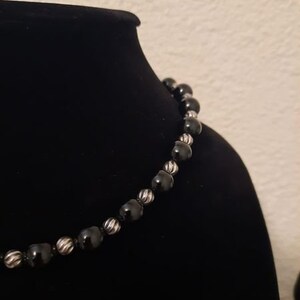 Peut inclure: Un collier de perles noires avec des accents argent&eacute;s. Les perles sont rondes et ont une surface l&eacute;g&egrave;rement textur&eacute;e.