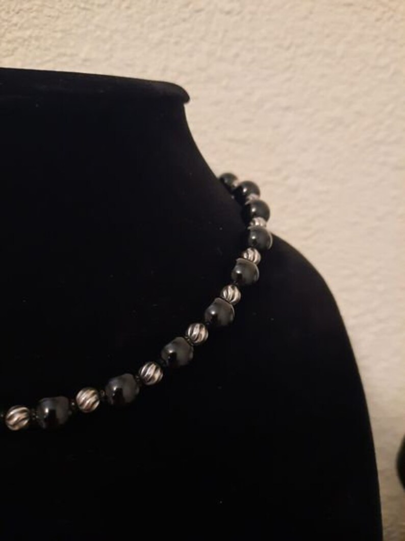 Peut inclure: Un collier de perles noires avec des accents argent&eacute;s. Les perles sont rondes et ont une surface l&eacute;g&egrave;rement textur&eacute;e.