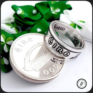 Op de afbeelding: Een zilveren ring gemaakt van een Ierse munt met het woord "Eire" gegraveerd rond de band. De ring ligt op een Ierse munt met het harp symbool en het woord "Eire" erop.