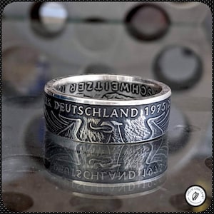 May include: A silver ring made from a 1975 German 5 Deutsche Mark coin. The ring features the German eagle and the inscription "DEUTSCHLAND 1975".