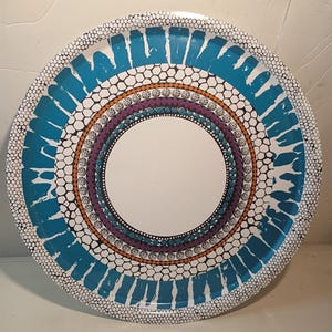May include: Circular decorative tray with a white central area and patterned borders. The borders display teal, purple, orange, and black designs, with a white dotted edge. The tray is probably made of metal.