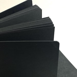 Puede incluir: Un diario de tapa dura negro con las p&aacute;ginas en abanico, mostrando el papel negro del interior.