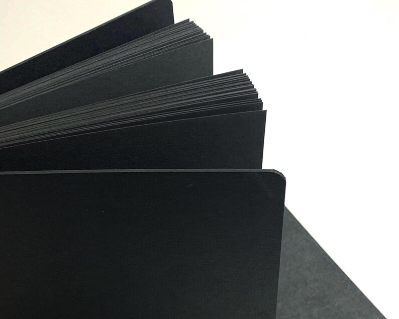 Puede incluir: Un diario de tapa dura negro con las p&aacute;ginas en abanico, mostrando el papel negro del interior.