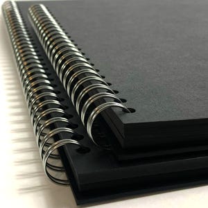 Puede incluir: Un cuaderno negro de espiral con una cubierta texturizada. El cuaderno est&aacute; cerrado y la encuadernaci&oacute;n es visible.