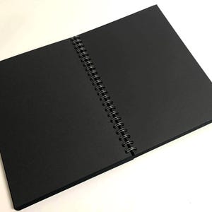 Puede incluir: Un cuaderno negro de espiral con una cubierta negra.