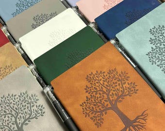 May include: A selection of notebooks in shades like blue, grey, and brown. Each notebook has an embossed tree design on the cover. Black pens are placed beside the notebooks. The notebooks are suitable for writing or journaling.