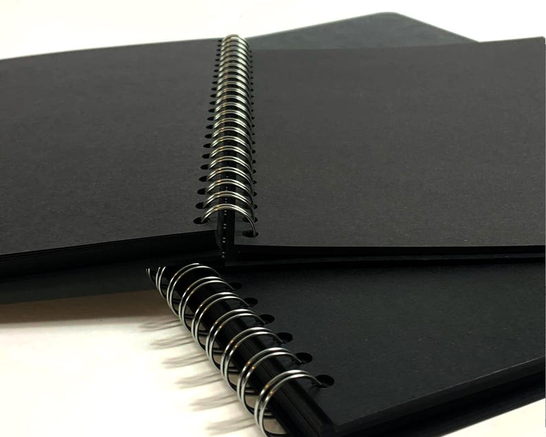 Puede incluir: Un cuaderno negro de espiral con una cubierta negra. El cuaderno est&aacute; cerrado y la encuadernaci&oacute;n es visible.