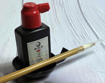 May include: A black ink bottle with a red cap, a calligraphy brush, and a small black inkwell. The ink bottle has a white label with Chinese characters. The brush is light brown with a clear tip.