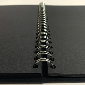 Puede incluir: Un cuaderno negro de espiral con una cubierta negra.