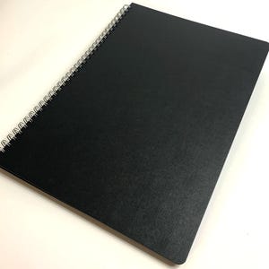 Puede incluir: Un cuaderno negro de espiral con una cubierta texturizada.