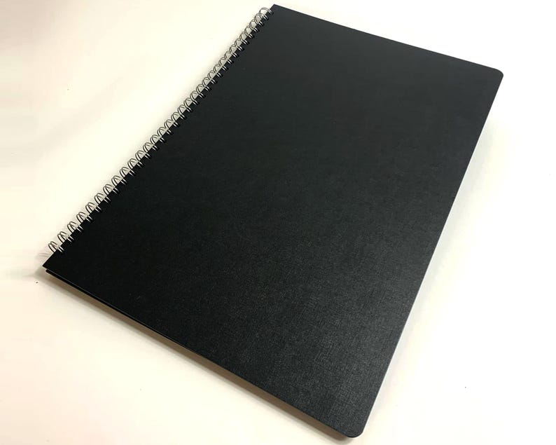 Puede incluir: Un cuaderno negro de espiral con una cubierta texturizada.