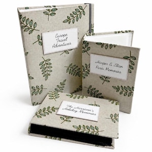Peut inclure: Trois albums photo avec des couvertures en lin beige ornées d'un motif de feuilles vertes. Chaque album porte une étiquette blanche avec les textes : "Europe Travel Adventures", "Harper & Stan Paris Memories", et "The Harrison's Holiday Memories".