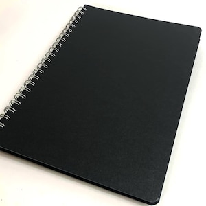 Puede incluir: Un cuaderno negro de espiral con una cubierta texturizada.