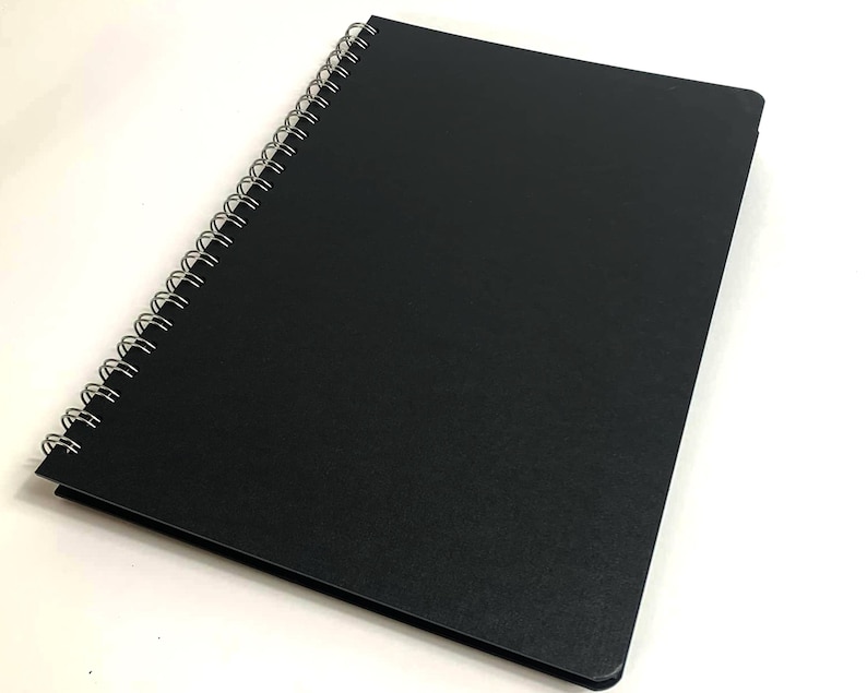 Puede incluir: Un cuaderno negro de espiral con una cubierta texturizada.