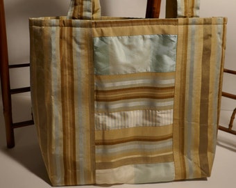 May include: A striped tote bag with a patchwork design in shades of brown, beige, and blue. The bag has two long straps.