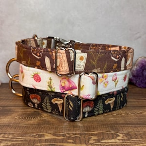 May include: Three stacked dog collars with various patterns. The top collar is brown with white illustrations. The middle collar is white with pink mushrooms and red strawberries. The bottom collar is black with mushrooms and ferns.