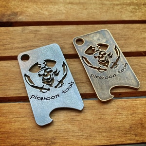 May include: Two metal bottle openers with a pirate skull design and the text "picaroon tools". One opener is silver and the other is gold.