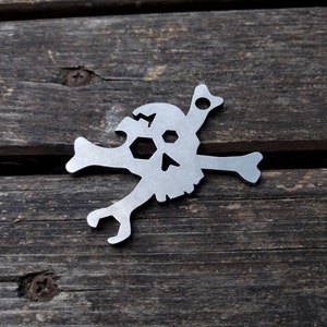 以下が含まれることがあります： ボトルオープナーとレンチが付いた、銀色の金属製のドクロとクロスボーンのキーホルダーです。