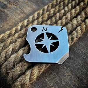 May include: A silver metal keychain with a compass design and a bottle opener. The compass features a star with four points and the letter "N" for north.